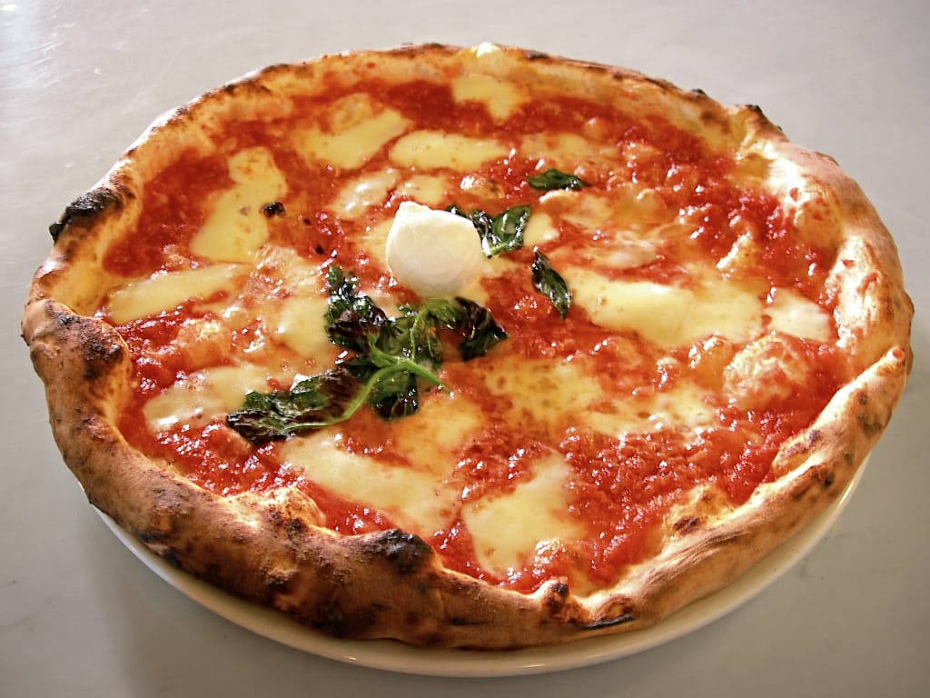 Neapolitan wood-fired margherita pizza with buffalo mozzarella and fresh basil, charred leopard-spotted crust