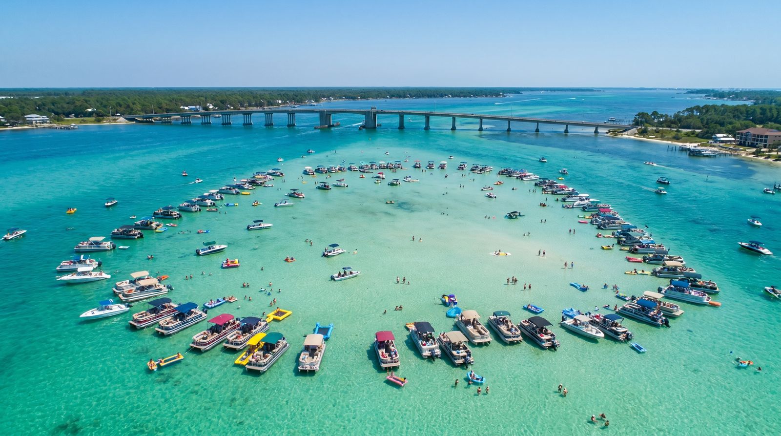 Group of vacationers on a pontoon boat anchored at Crab Island sandbar Destin with emerald green shallow water all around them