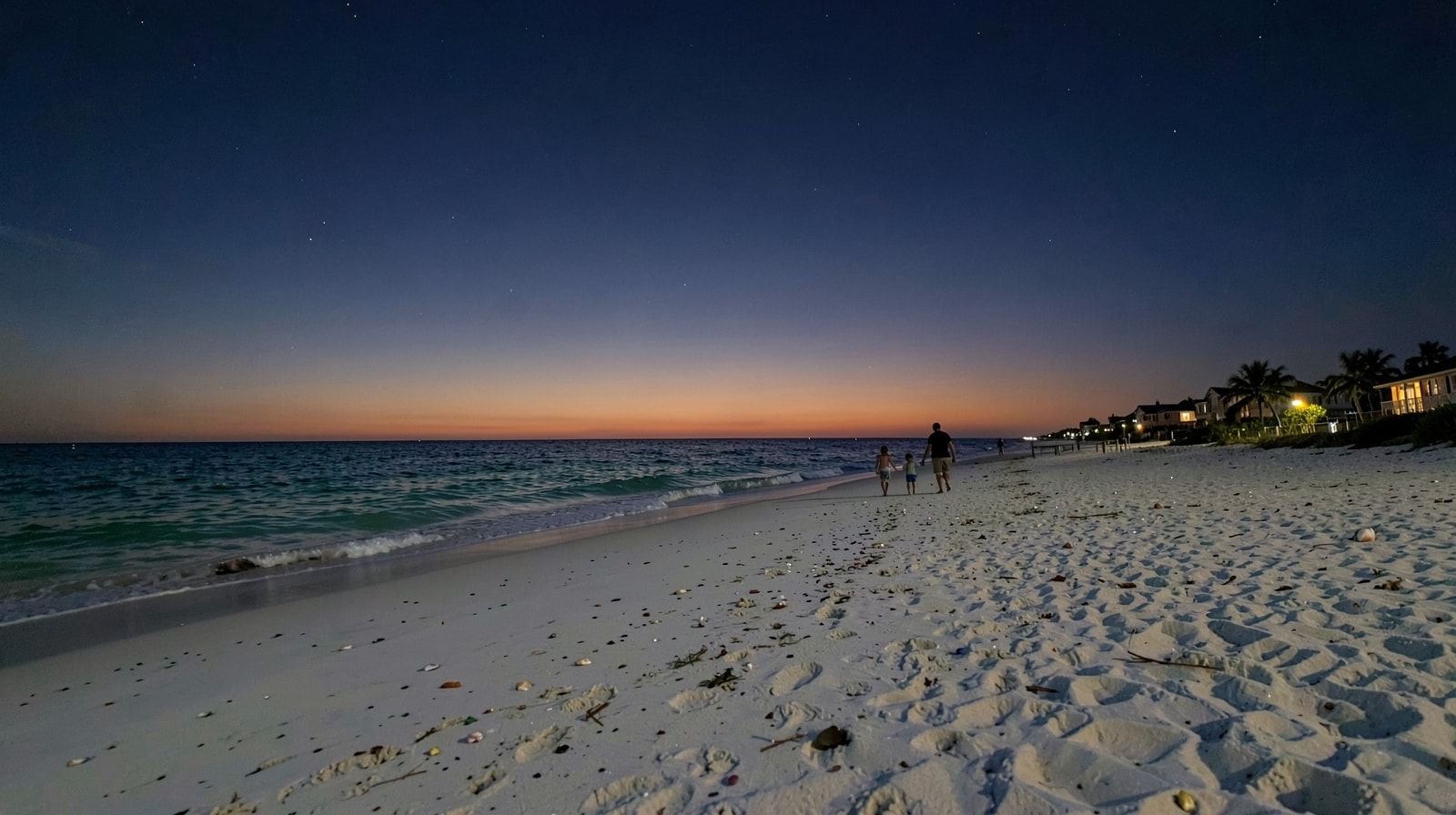 Quiet Destin Florida beach at twilight with deep indigo sky and a small family walking at the Gulf waterline in the distance