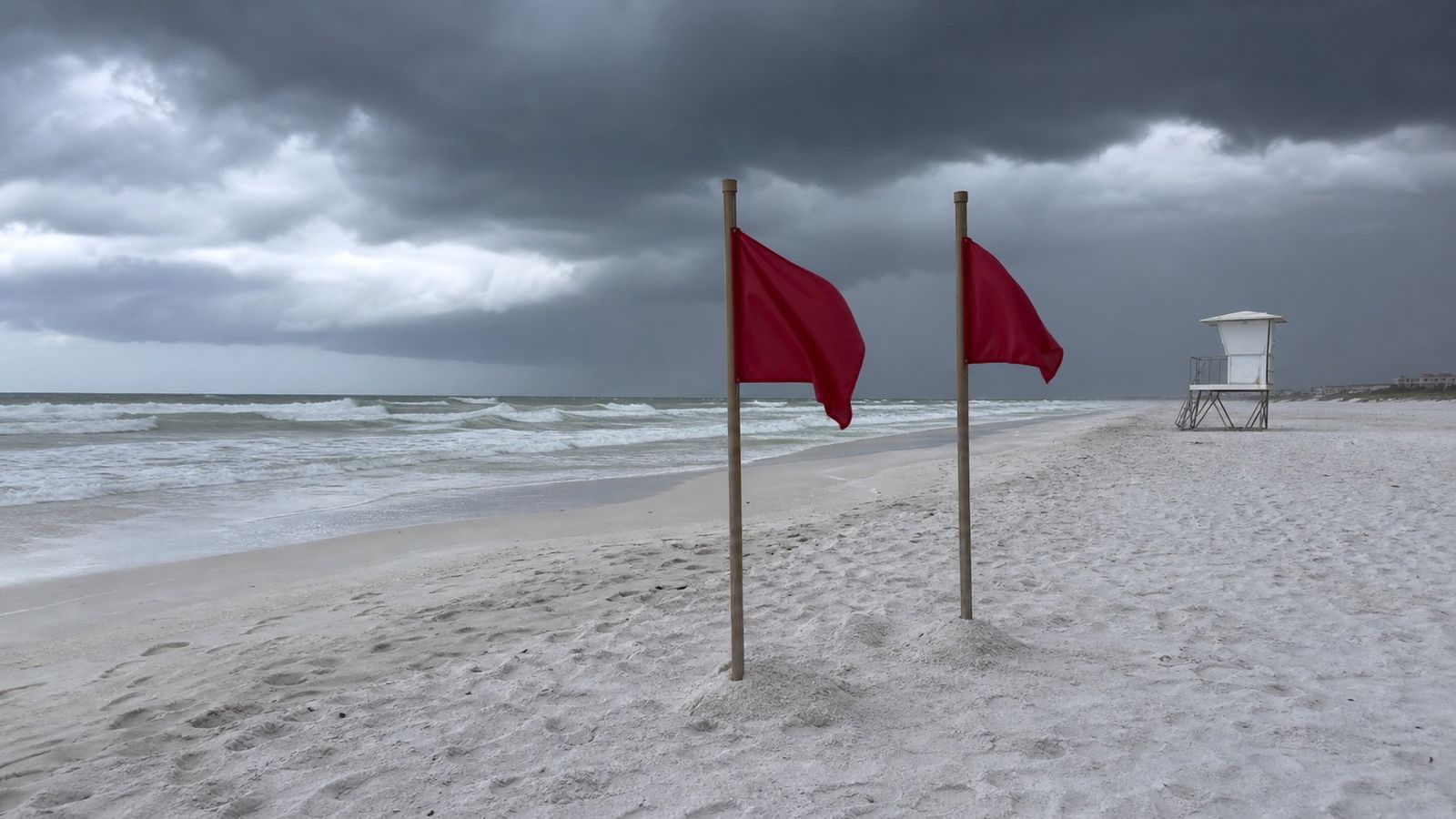 Double red warning flags in the white sand at a Destin Florida beach with rough surf and no swimmers