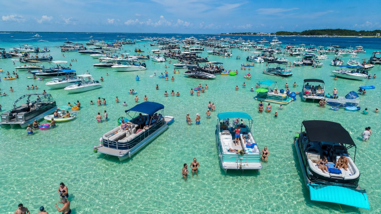Crab Island sandbar in Destin Florida harbor with dozens of colorful boats anchored in shallow clear emerald water and people wading
