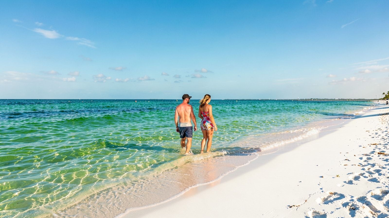 Couple wading in clear emerald-green Gulf of Mexico water on the white sand beach at Destin Florida