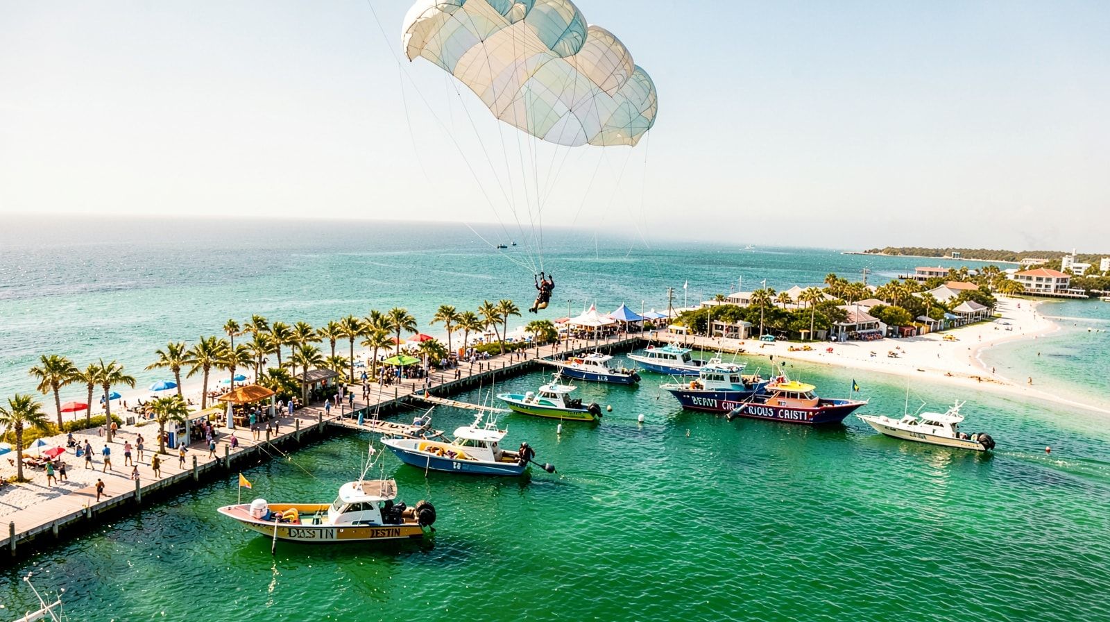 Parasailing above Destin Harbor with charter fishing boats and waterfront boardwalk