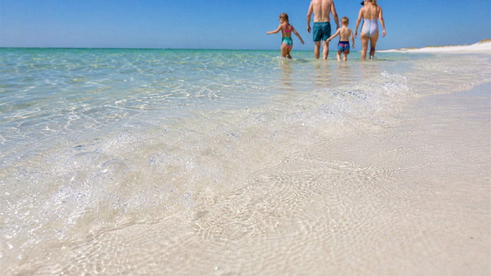 Crystal-clear emerald Gulf water lapping the white quartz sand beach at Destin Florida with a family wading