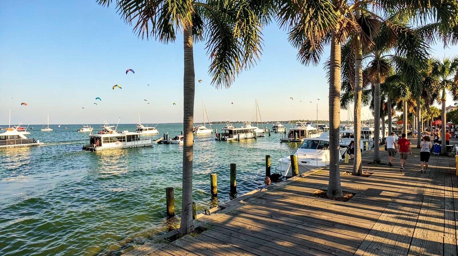 Busy summer afternoon on Destin Harbor Florida with charter fishing boats moored along a boardwalk and colorful parasails rising over the emerald Gulf water