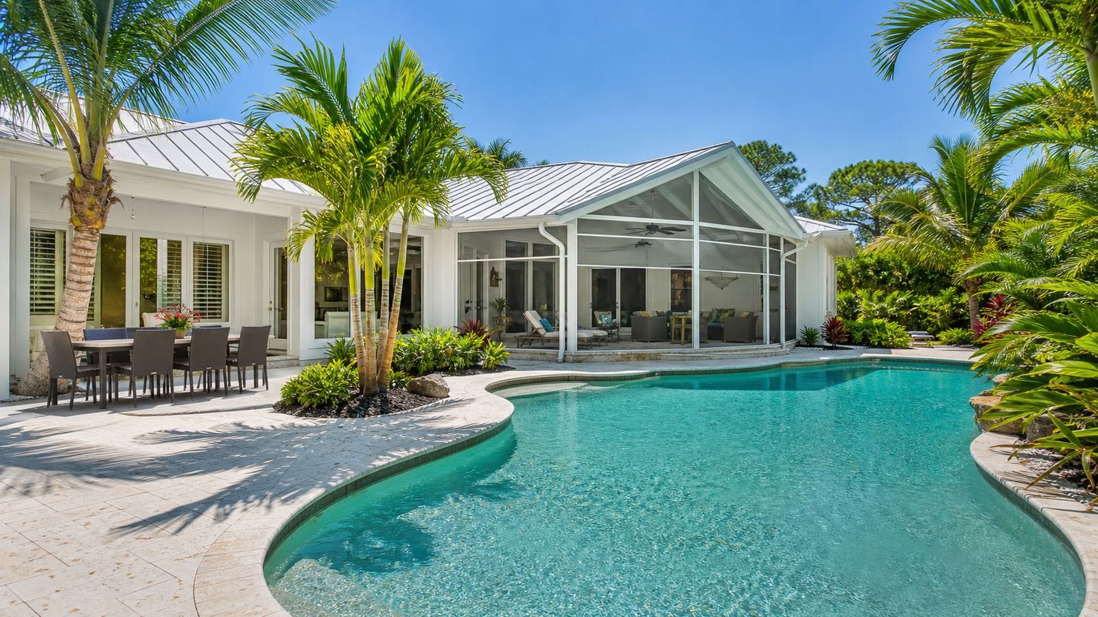 Florida Gulf Coast vacation rental home with private pool and outdoor dining area surrounded by palm trees on a sunny afternoon