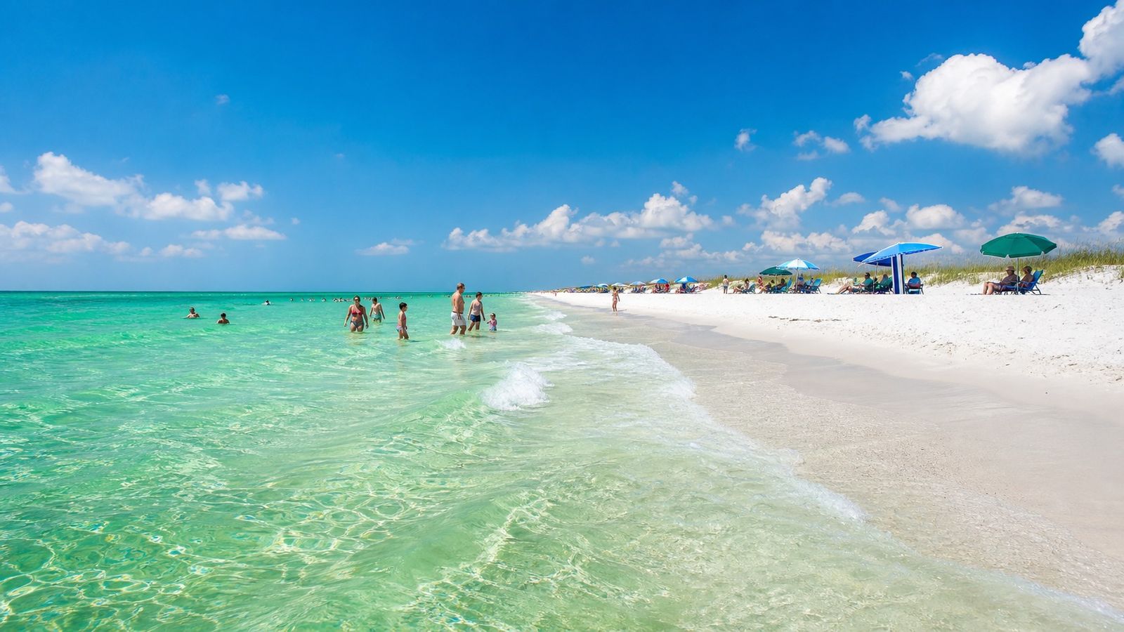 Vivid emerald-green Gulf water at a white-sand Florida Panhandle beach with families wading in the shallows