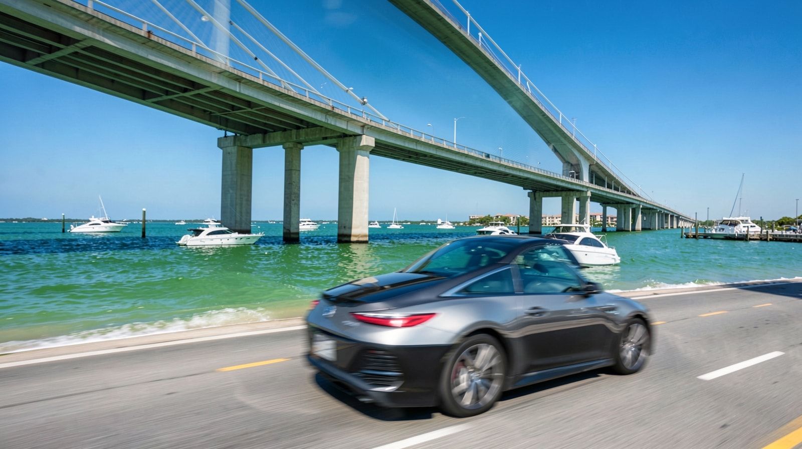 Car crossing a harbor bridge over emerald green water in Destin Florida with white charter boats and a bright blue sky
