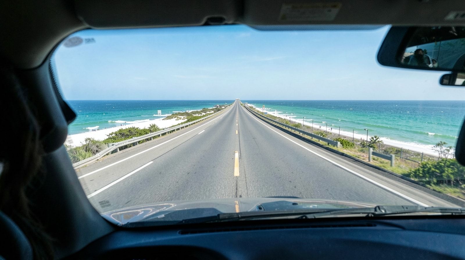 View from inside a car on a road trip looking through the windshield at a long straight interstate highway stretching toward the horizon
