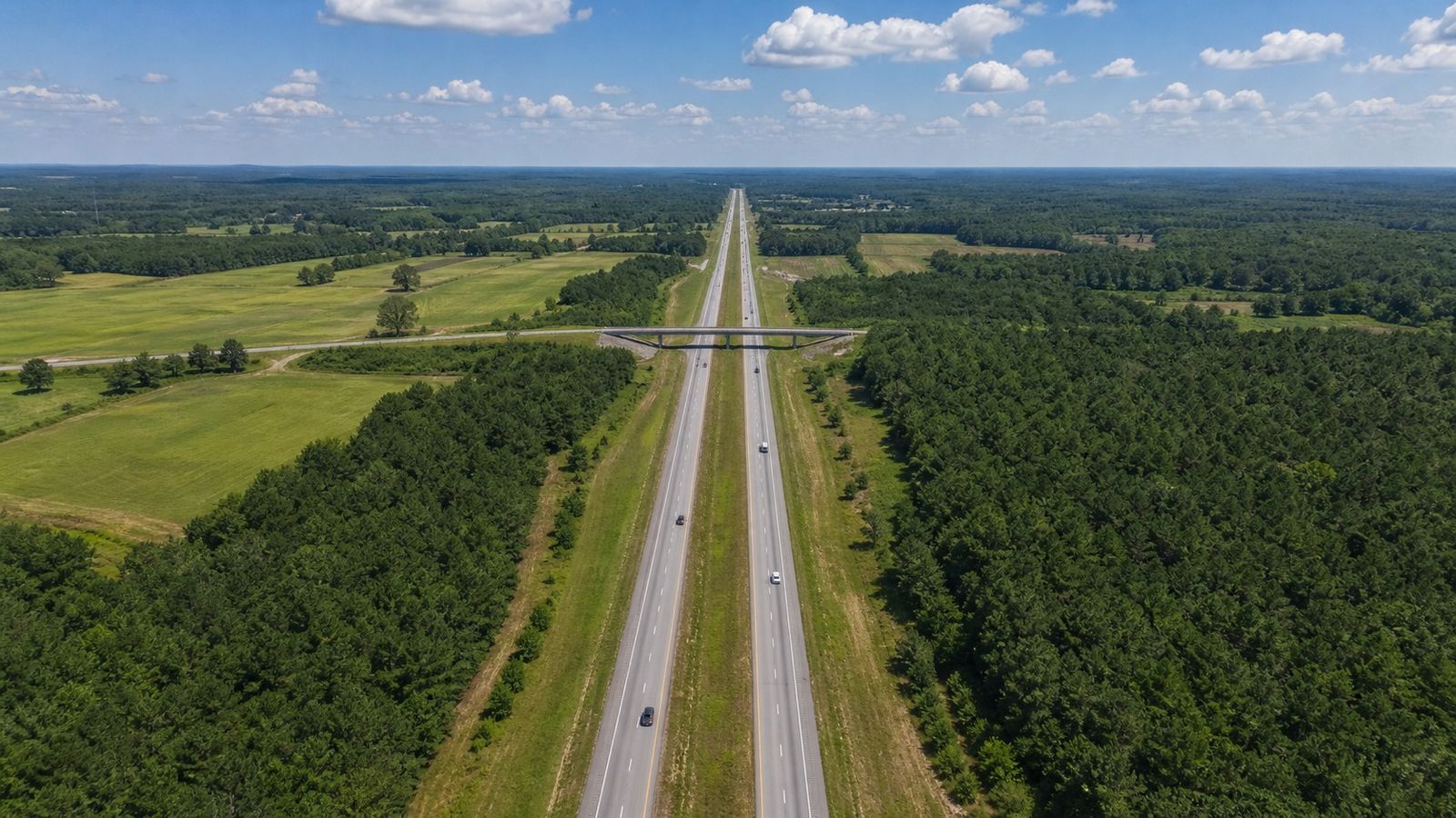 Aerial view of a Mississippi interstate highway cutting south through pine forest and farmland toward the Gulf Coast on a sunny day