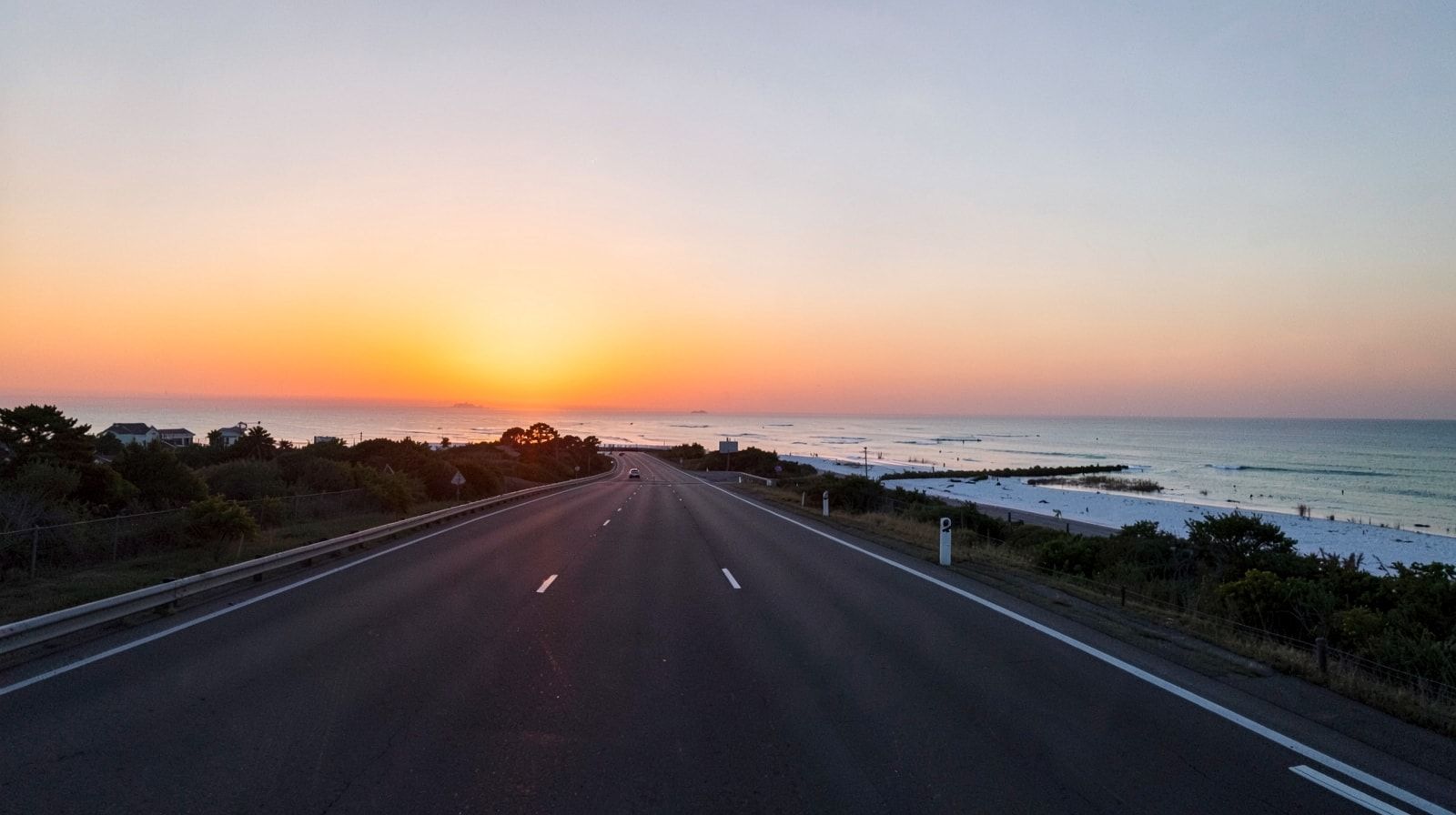 Empty wide interstate highway at pre-dawn with a soft orange sunrise glowing on the horizon