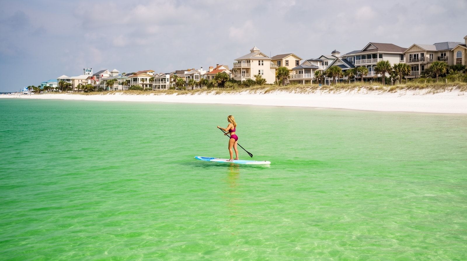 Woman stand-up paddleboarding on calm emerald Gulf water near Destin Florida in October with clear water and white sand visible below